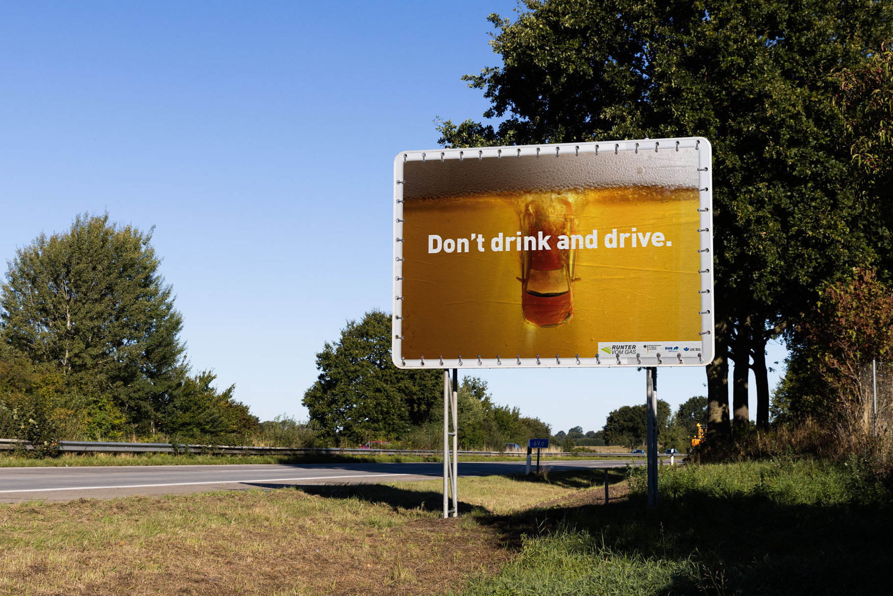 Autobahnplakat rechts neben Fahrbahn mit dem Text: Don't trink and drive. Als Hintergrund ist ein Getränk mit Schaum zu sehen 